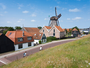 village of oudeschild with windmill on dutch island of texel seen from dike - obrazy, fototapety, plakaty