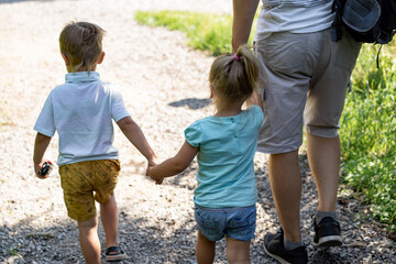 backview of man walking alone lane in park with children holding daughter by hand