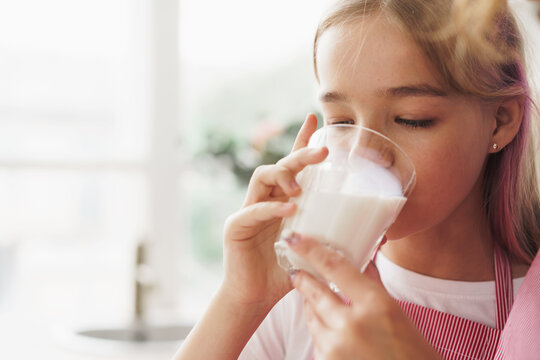 Blonde teen girl drinking glass of milk at home in kitchen