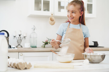 Obraz na płótnie Canvas Portrait of a little blonde teen girl wearing apron in kitchen