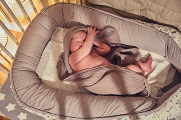 A newborn baby sleeps in a crib with a cocoon and a blanket in the form of a turban on his head