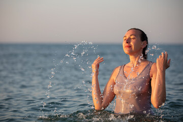 A middle-aged woman stands in the sea and splashes water.