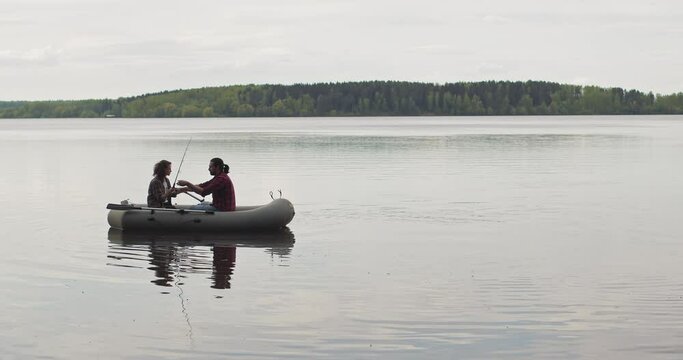Young fishermen on an inflatable boat on the lake are fishing. Cinematic shot.