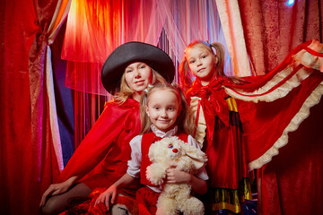 Fototapeta premium Family during a stylized theatrical circus photo shoot in a beautiful red location. Models mother and daughter posing on stage with curtain