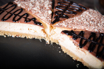 Sliced cheesecake with cocoa and chocolate sauce close-up on the table, studio photo.