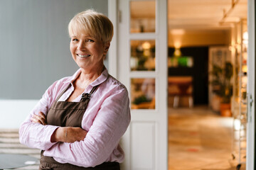 White mature woman standing and smiling at camera in cafe outdoors