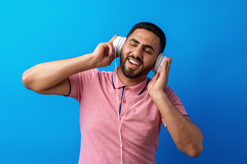 Young happy arab man with headphones listening to music against blue background
