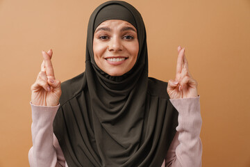 Young muslim woman in hijab holding fingers crossed for good luck