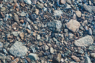 Smooth stones at bottom shallow mountain stream, rocky background close-up. Sun glare on smooth...