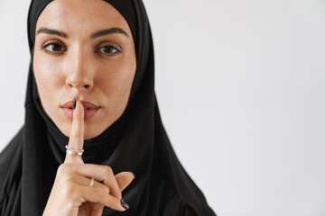 A portrait of the muslim woman in hijab showing a silence gesture in the white studio