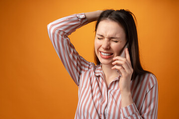 Stressed frustrated young woman holding smartphone, recieved bad news, yellow background