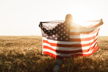 Young man holding American flag on back while standing in wheat field