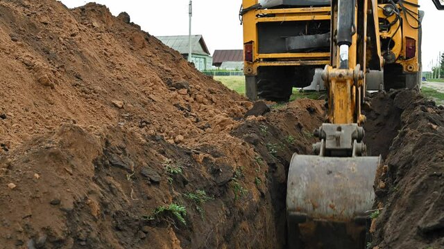 Close up of an excavator digging a deep trench. An excavator digs a trench in the countryside to lay a water pipe. Summer cloudy day