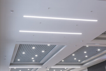 suspended and grid ceiling with halogen spots lamps and drywall construction in empty room in store or house. Stretch ceiling white and complex shape. - obrazy, fototapety, plakaty