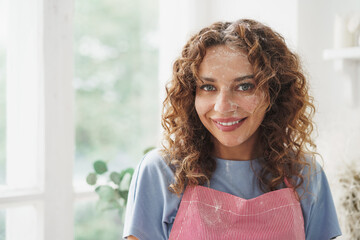 Smiling woman in apron standing in kitchen with face dirty in flour