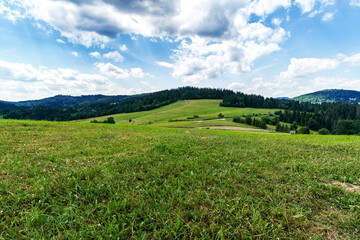 Rolling landscape with meadows, forest covered hills and blue sky with clouds