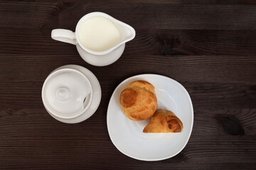 Profiteroles on white plate and tea set on wooden background. Top view. Baking for tea