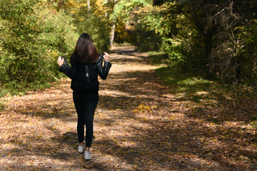 Lonely young woman with dark hair walk through the forest. Girl outdoor, sunny park. Back view
