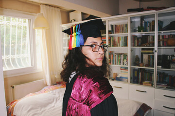 Portrait of young woman with graduation cap & gown and tassels arranged as lgbtq rainbow pride flag...