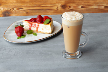 Glass of latte coffee and piece of strawberry cheesecake on gray table