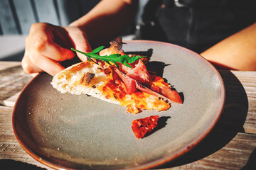 woman Hand takes a slice of meat neapolitan Pizza with Mozzarella cheese, ham, bacon, tomato, Spices and jalapeno on plate in cafe outdoor