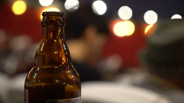 Beer bottle with very shallow clear depth of field in the foreground with very blurry people images and smooth bokeh in the background