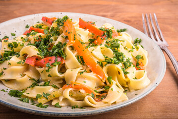 Pasta with cream sauce with bell pepper on a plate, close-up - fettuccine with bell pepper, sprinkled with chopped parsley