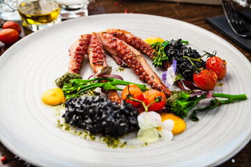 Octopus with black risotto. Carrot cream, mini-broccoli, basil pesto. Delicious healthy traditional food closeup served for lunch in modern gourmet cuisine restaurant