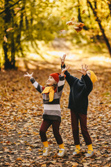 Happy funny children friends brother and sister in warm bright clothes walking having fun catching leaves in the park in autumn in nature, selective focus