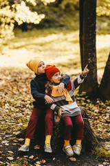 Happy playful children friends in warm clothes a hat in bright hats and scarves are walking having fun sitting on a stump and a pumpkin catching leaves in the autumn forest in nature, selective focus