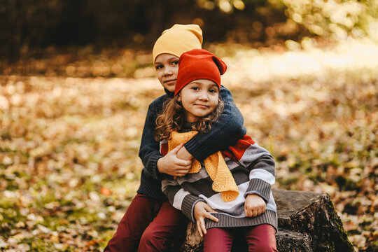 Happy playful children friends in warm clothes a hat in bright hats and scarves are walking having fun sitting on a stump and a pumpkin catching leaves in the autumn forest in nature, selective focus