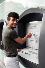 Portrait of a young African American man smiling while holding his credit card and inserting it...