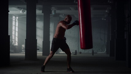 Man hitting punch bag during intense workout. Male boxer practicing kickboxing
