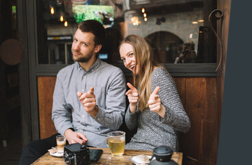 Optimistic couple pointing at camera having fun in cafe