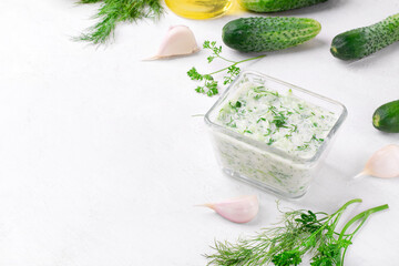 Tzatziki, cucumber sauce with yogurt, garlic, olive oil, herbs and lemon juice on the white table. Greek sauce