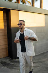 Chico joven atractivo vestido a la moda posando delante de una casa