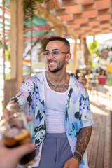 Chico joven atractivo tatuado con camisa de flores en bar de playa en verano