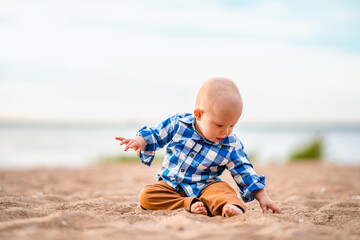 Cute baby boy sitting on the sand on the beach at sunset