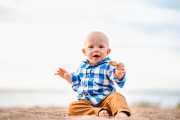 Cute baby boy sitting on the sand on the beach at sunset