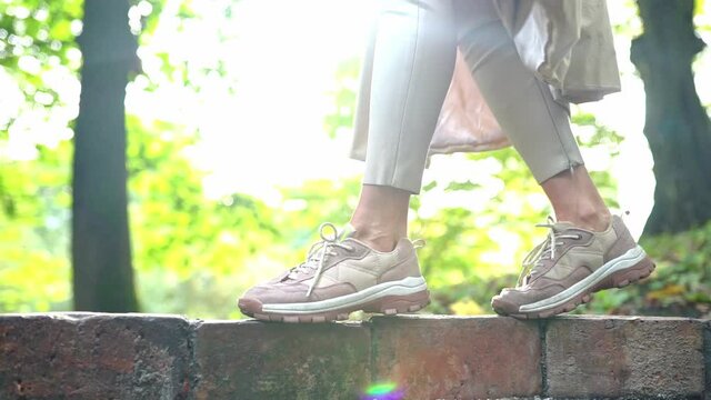 Low view of female feet in sneakers steps by brick fense. Close up. Slow motion