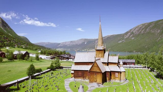 Front Exterior Of Lom Stave Church Overlooking Mountain And Otta River at Daytime In Norway. - aerial