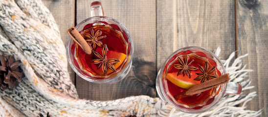 banner with two cups with mulled wine on wooden table with warm knit woolen scarf and fir cones....