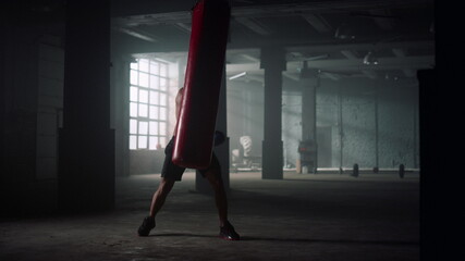 Fototapeta na wymiar Boxer kicking punch bag during training. Man practicing kicks on sports bag