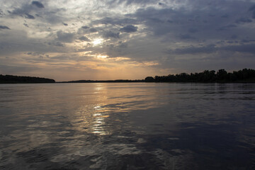 Obraz premium Red sunset on the river. Evening. The rays of the sun in the clouds