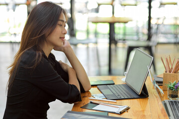 Fototapeta premium Attractive woman thinking about her job with smart tablet at coffee shop co-working area