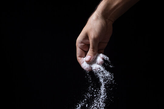 Salt On A Black Background. Hand Sprinkles Salt On Dark Background