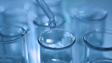 Dropping chemical liquid to test tubes for lab testing, science laboratory research and development concept, blue tone