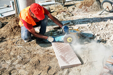 Pavement construction worker using an angle grinder for cutting the tiles