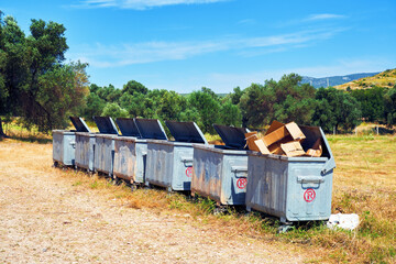 Fototapeta na wymiar Metal garbage containers in a row in a rural field