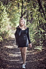 Sexy Young woman in a little black dress and biker jacket walking In Forest During Autumn.
